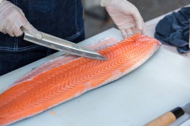 Somon, deneyimli şefin elinde. Sashimi ve suşi için somon filetosu dilimlemek için bıçak kullanıyor. Bir şef somon filetosunu kesme tahtasındaki bıçakla kesiyor. Balık filetosu. 