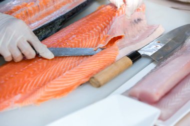 Somon, deneyimli şefin elinde. Sashimi ve suşi için somon filetosu dilimlemek için bıçak kullanıyor. Bir şef somon filetosunu kesme tahtasındaki bıçakla kesiyor. Balık filetosu.