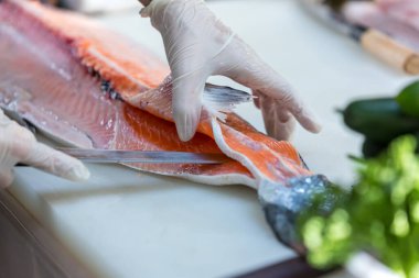 Somon, deneyimli şefin elinde. Sashimi ve suşi için somon filetosu dilimlemek için bıçak kullanıyor. Bir şef somon filetosunu kesme tahtasındaki bıçakla kesiyor. Balık filetosu.