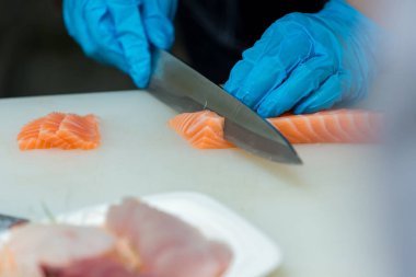 Somon, deneyimli şefin elinde. Sashimi ve suşi için somon filetosu dilimlemek için bıçak kullanıyor. Bir şef somon filetosunu kesme tahtasındaki bıçakla kesiyor. Balık filetosu. 