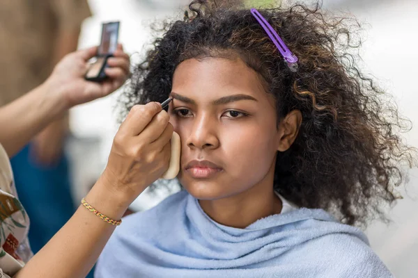 Stylist is putting make up on black woman eyebrows with the eyebrows brush. Make up artist stylist apply  the eyebrows with brush makes the model is natural makeup