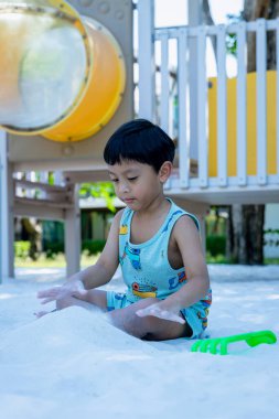 Küçük Çocuk kum havuzunda oyun parkında. Yazın çocuk oyun alanında kum oynuyor. Çocuk kum havuzunda oturuyor ve parkta oynuyor. 