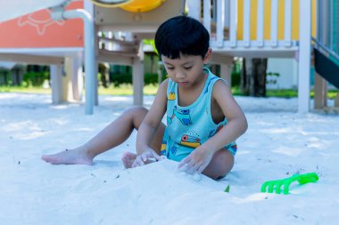 Küçük Çocuk kum havuzunda oyun parkında. Yazın çocuk oyun alanında kum oynuyor. Çocuk kum havuzunda oturuyor ve parkta oynuyor. 