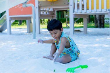 Küçük Çocuk kum havuzunda oyun parkında. Yazın çocuk oyun alanında kum oynuyor. Çocuk kum havuzunda oturuyor ve parkta oynuyor. 