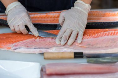 Somon, deneyimli şefin elinde. Sashimi ve suşi için somon filetosu dilimlemek için bıçak kullanıyor. Bir şef somon filetosunu kesme tahtasındaki bıçakla kesiyor. Balık filetosu.