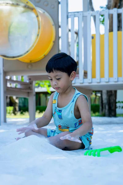 Küçük Çocuk kum havuzunda oyun parkında. Yazın çocuk oyun alanında kum oynuyor. Çocuk kum havuzunda oturuyor ve parkta oynuyor. 