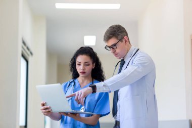 Üniformalı klinisyenler ayakta dikilip bilgisayar monitörlerine bakıyor, tıbbi belgeleri tartışıyor ve danışmanlık yapıyorlar. Doktor ve hemşire tıp bürosunda dizüstü bilgisayarla çalışıyorlar. Dizüstü bilgisayarla profesyonel tıbbi işler.