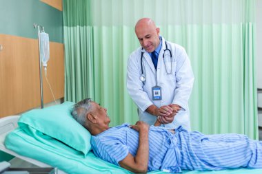 Doktor, koğuştaki hastayı ziyaret ediyor. Hastanede yatan adam doktorunu kontrol ederken yatakta yatıyor. Hastane odasında erkek hastayı muayene eden bir doktor.