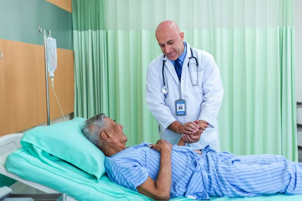 Doktor, koğuştaki hastayı ziyaret ediyor. Hastanede yatan adam doktorunu kontrol ederken yatakta yatıyor. Hastane odasında erkek hastayı muayene eden bir doktor.