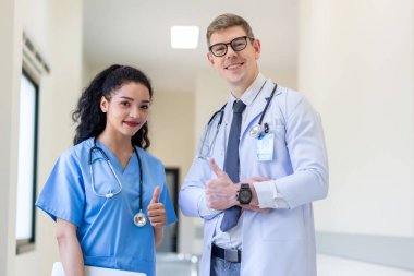 Üniformalı klinisyenler ayakta dikilip bilgisayar monitörlerine bakıyor, tıbbi belgeleri tartışıyor ve danışmanlık yapıyorlar. Doktor ve hemşire tıp bürosunda dizüstü bilgisayarla çalışıyorlar. Dizüstü bilgisayarla profesyonel tıbbi işler.