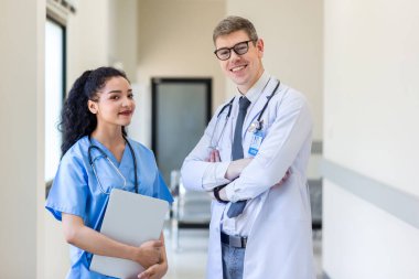 Üniformalı klinisyenler ayakta dikilip bilgisayar monitörlerine bakıyor, tıbbi belgeleri tartışıyor ve danışmanlık yapıyorlar. Doktor ve hemşire tıp bürosunda dizüstü bilgisayarla çalışıyorlar. Dizüstü bilgisayarla profesyonel tıbbi işler.