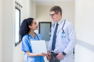 Üniformalı klinisyenler ayakta dikilip bilgisayar monitörlerine bakıyor, tıbbi belgeleri tartışıyor ve danışmanlık yapıyorlar. Doktor ve hemşire tıp bürosunda dizüstü bilgisayarla çalışıyorlar. Dizüstü bilgisayarla profesyonel tıbbi işler.