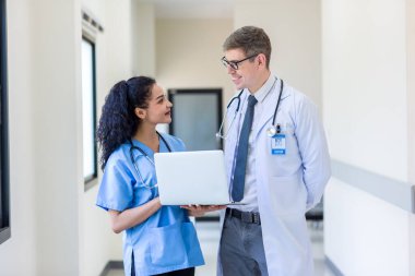 Üniformalı klinisyenler ayakta dikilip bilgisayar monitörlerine bakıyor, tıbbi belgeleri tartışıyor ve danışmanlık yapıyorlar. Doktor ve hemşire tıp bürosunda dizüstü bilgisayarla çalışıyorlar. Dizüstü bilgisayarla profesyonel tıbbi işler.