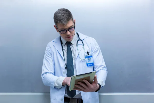 Doctor holding tablet at hospital. Friendly male doctor dressed in uniform holding tablet.