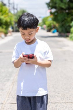 Çocuk ayakta duruyor ve mobil ve sosyal medya kullanıyor. Çocuk onunla oynuyor. Akıllı telefon.