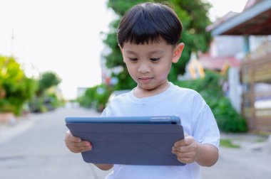 Çocuk ayakta duruyor ve tablet ve sosyal medya kullanıyor. Çocuk dijital tabletle oynuyor