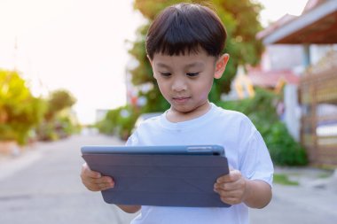 Çocuk ayakta duruyor ve tablet ve sosyal medya kullanıyor. Çocuk dijital tabletle oynuyor