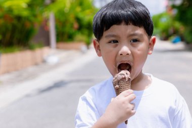 Çocuk çikolatalı dondurma yerken eğleniyor. Küçük çocuk dışarıda dondurma yiyor.