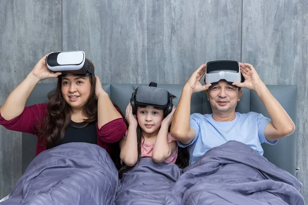 Family time using VR glasses together on bed at home for gaming or learning.