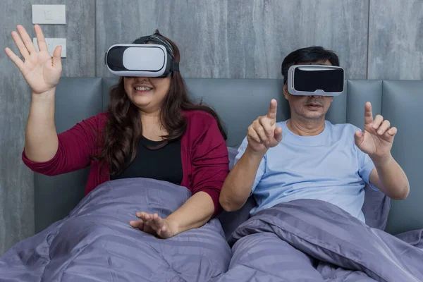 Family time dad and mom using VR glasses together on bed at home for gaming or learning.