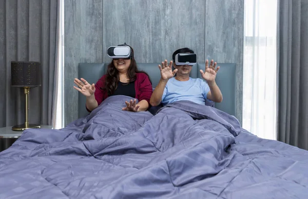 Family time dad and mom using VR glasses together on bed at home for gaming or learning.