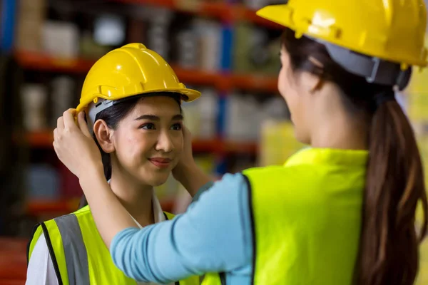 Woman puts a safety helmet on woman at factory or plant site. Business heir concept. Happy lover wearing safety helmet on together