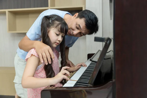 Father and daughter at home playing music on a piano. Dad and daughter are playing the piano. Pianist teacher teaching girl kid student to play piano, music education concept.