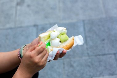 The scoops of ice cream are put in the bread. Ice cream with bread Thai street food. A soft bread topped with scoop of ice cream on Hand.