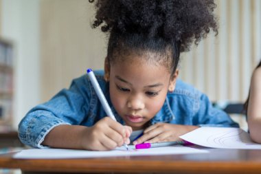 Girl is doing homework in the Classroom. Back to school! Cute industrious children are sitting at desks indoors. Kids are learning in class.
