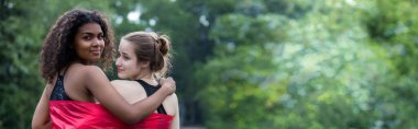 Two  young women standing with a pride rainbow flag. couple hugging at outdoor. LGBT rainbow flag.