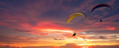 Paraşütçü paraşütçülerin hava dalışı ve gün batımı manzarası. Güneş batmış, uçan siluet. Akşam gökyüzünde gün batımıyla uçan paraglider silueti..