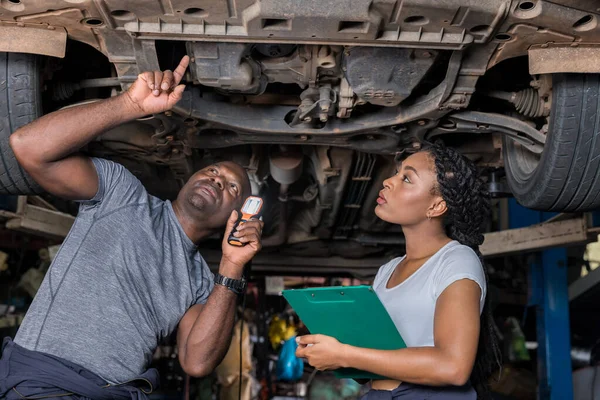 Professional Car Mechanic is Investigating Under a Vehicle on a Lift in Service. Auto Service Worker Checking Car Under Carriage Look For Issues. Car service technician check and repair customer car.