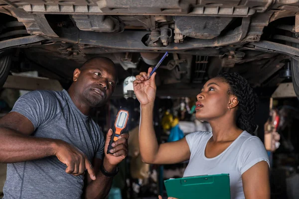 Professional Car Mechanic is Investigating Under a Vehicle on a Lift in Service. Auto Service Worker Checking Car Under Carriage Look For Issues. Car service technician check and repair customer car.