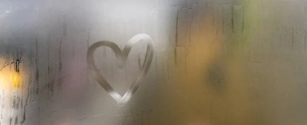 A heart painted on a misted window. Heart on misted glass. Heart on a window background. Heart symbol of love drawn on the glass.