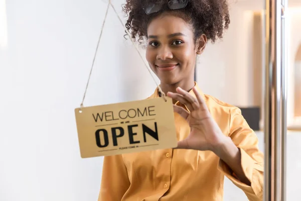 Woman store owner turning open sign broad through the door glass and ready to service. Small business woman owner turning the sign for the reopening