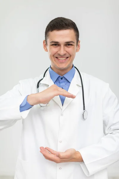 Um médico sorrindo está à frente e tem as mãos levantadas para anunciar um novo produto. — Fotografia de Stock