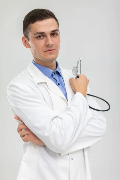 Doktor se dívá do kamery a drží v ruce stetoskop. Neutrální obličej. — Stock fotografie