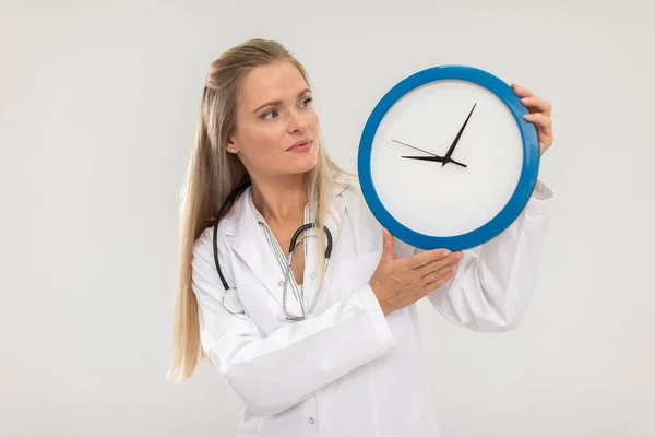 Die Ärztin hält eine Wanduhr in der Hand und erinnert Sie daran, dass es Zeit ist, zu behandeln. — Stockfoto