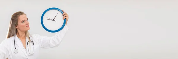 El médico sostiene un reloj de pared en sus manos y nos recuerda que es hora de tratar. Marco panorámico. —  Fotos de Stock