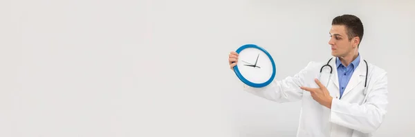 El médico sostiene un reloj de pared en sus manos midiendo el tiempo diario. Vista panorámica. —  Fotos de Stock