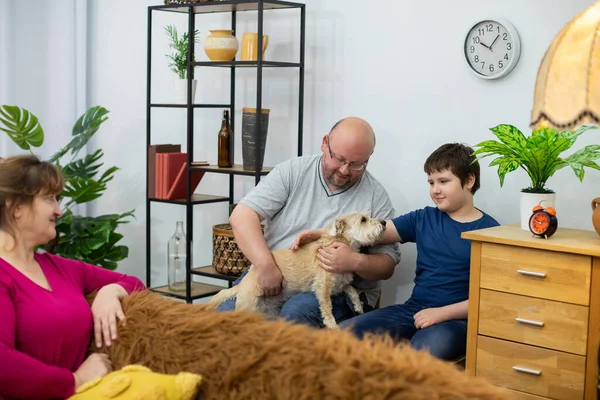 Um pai e um filho sentam-se em cadeiras contra a parede e seguram um cão desgrenhado em suas voltas. — Fotografia de Stock