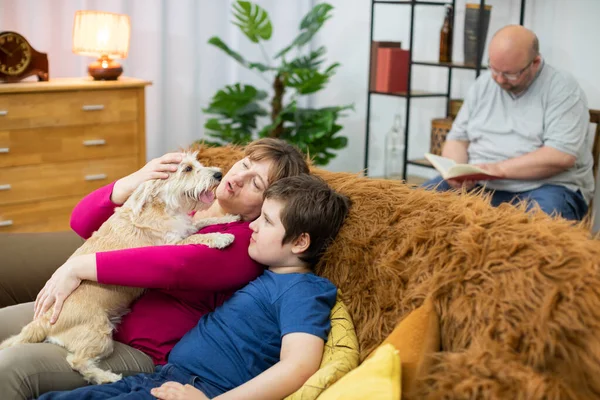 Mãe e filho estão sentados no sofá e segurando um cachorro em seus braços. O pai está lendo um livro. — Fotografia de Stock