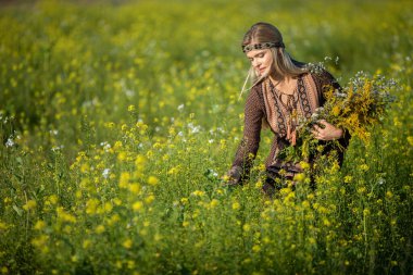Bir şifalı ot uzmanı ekilmiş kolza tarlalarını kontrol ediyor. Elinde bir buket bitki tutuyor..