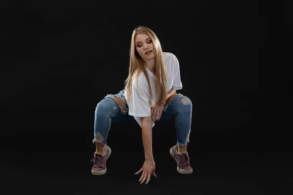 A young dancer crouches and supports herself with one hand and looks down. Long blonde hair. — Stock Photo, Image