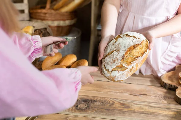Uma jovem paga em dinheiro por pães selecionados na padaria da empresa. Vendedora atraente na padaria familys loja da empresa. — Fotografia de Stock