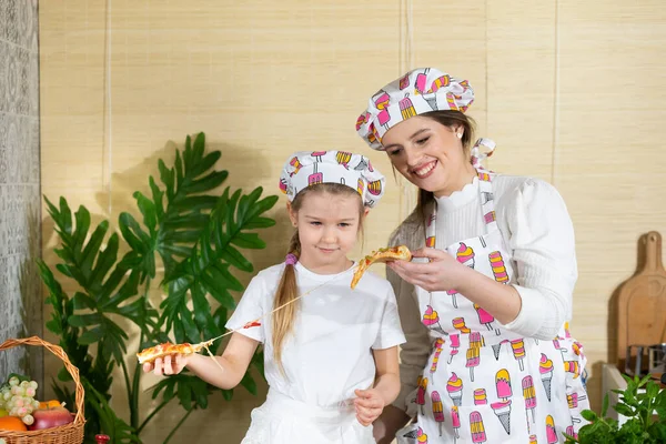 Atrakcyjna matka z pięcioletnią córką oddziela kawałki pizzy, które sami upiekli i chcą spróbować. Puki jest gorąca i pachnąca. Po wspólnej pracy w kuchni — Zdjęcie stockowe