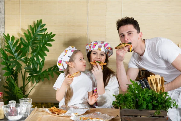 The five-year-old daughter sat down on her mothers lap and my dad joined his wife and they were eating pizza made and baked by them. After working together in the kitchen, its time to eat together.