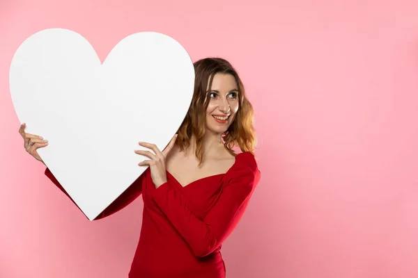 Chica con una gran forma de corazón blanco en las manos. Una estudiante enamorada se para y sostiene una gran forma de corazón en sus manos. Día de San Valentín y amor. — Foto de Stock