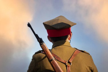 Sırtında tüfeği olan bir asker bulutlu bir gökyüzüne karşı.