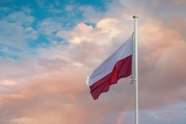 Государственный флаг Польши развевается на фоне голубого неба и персиковых облаков. — стоковое фото